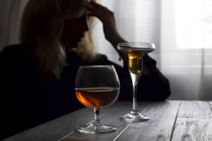Woman drinking alcohol alone looking out her window. Depression, alcoholism, lonely person concept. Alcohol addiction and Social problem - with alcoholism and poisoning